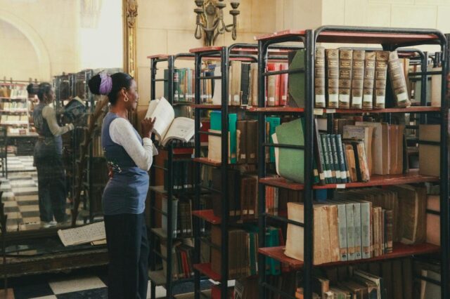 A woman exploring bookcases in a classic library setting, immersed in reading.
