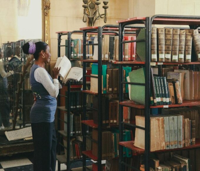 A woman exploring bookcases in a classic library setting, immersed in reading.