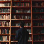 A man with short black hair stands in front of bookshelves in a quiet library.