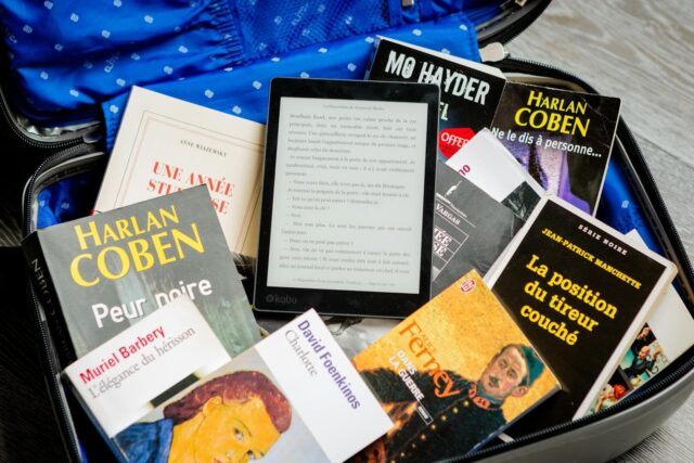 A mix of paperback books and an e-reader neatly packed in an open suitcase for travel.