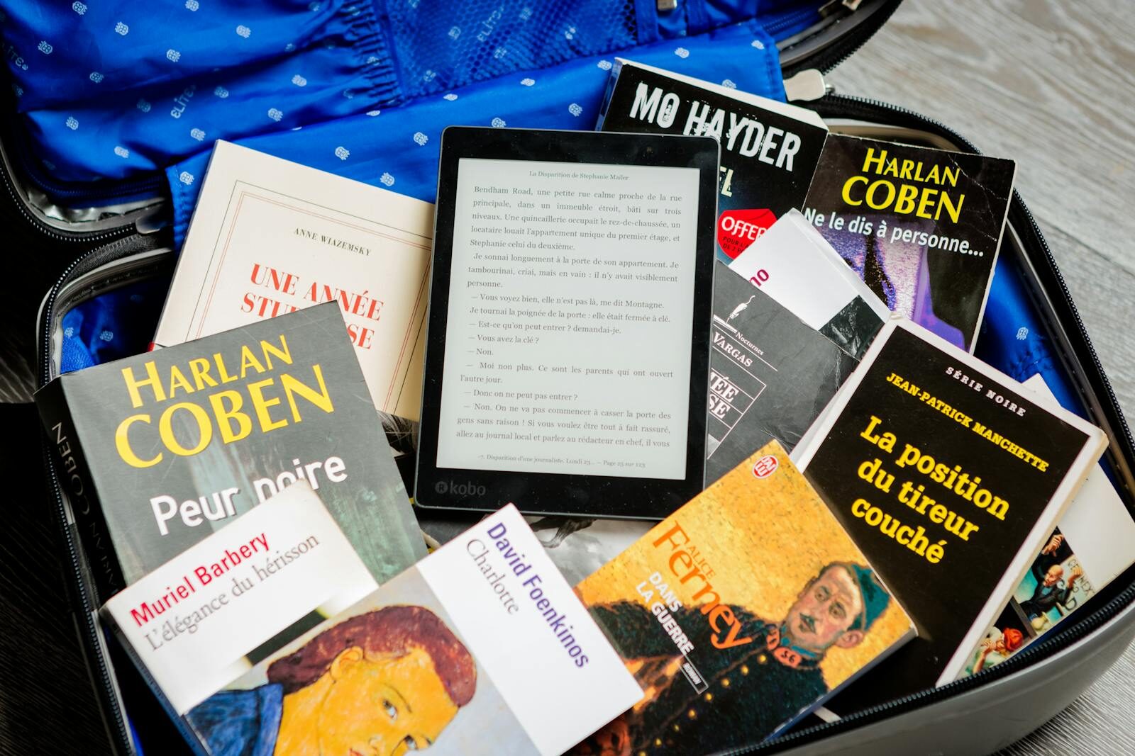 A mix of paperback books and an e-reader neatly packed in an open suitcase for travel.