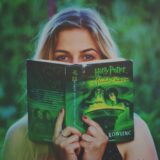 A woman reading a Harry Potter book amidst greenery, enjoying leisure time.