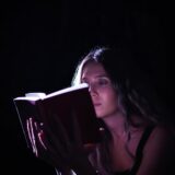 A woman absorbed in a book, illuminated by focused light, creating a dramatic effect.