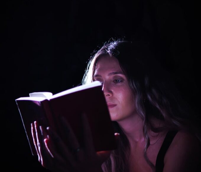 A woman absorbed in a book, illuminated by focused light, creating a dramatic effect.