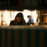 Two women immersed in study within a quiet, cozy library environment.