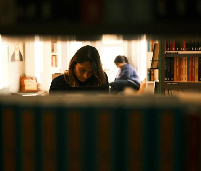 Two women immersed in study within a quiet, cozy library environment.