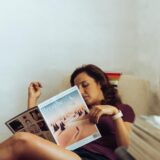 A woman comfortably relaxing at home, reading a magazine on the sofa.