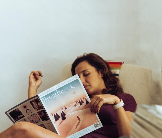 A woman comfortably relaxing at home, reading a magazine on the sofa.