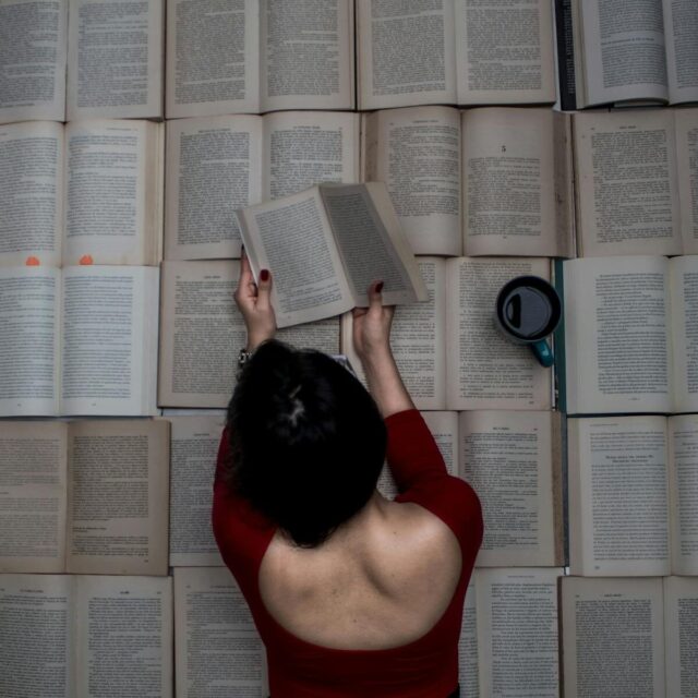 A woman engrossed in reading while surrounded by open books and a mug of coffee.