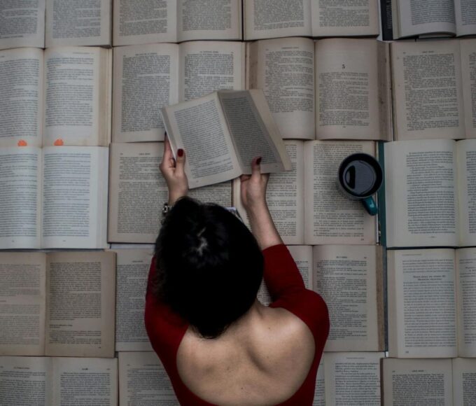 A woman engrossed in reading while surrounded by open books and a mug of coffee.