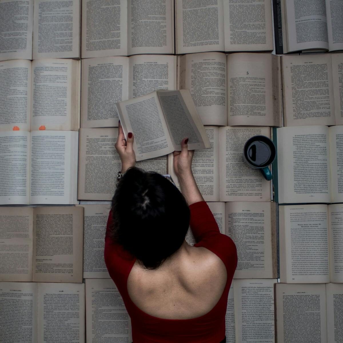 A woman engrossed in reading while surrounded by open books and a mug of coffee.