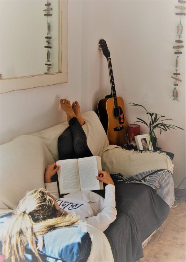 Woman relaxing on a sofa reading a book with an acoustic guitar in the background.