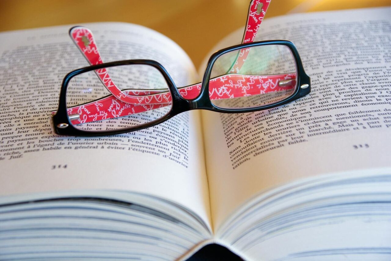 Eyeglasses resting on an open book reflecting text for a concept of literature and learning.
