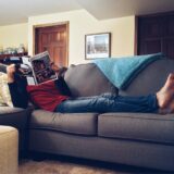 Person relaxing on a comfortable sofa reading a magazine in a cozy living room.
