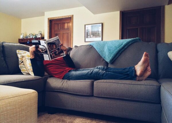 Person relaxing on a comfortable sofa reading a magazine in a cozy living room.