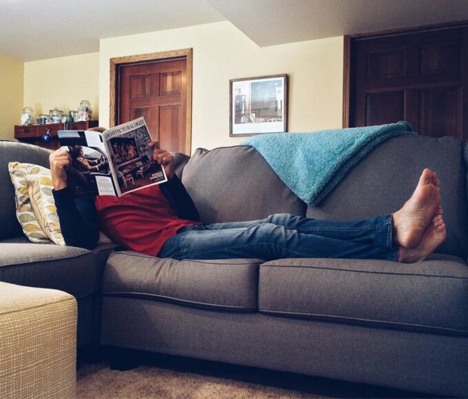 Person relaxing on a comfortable sofa reading a magazine in a cozy living room.