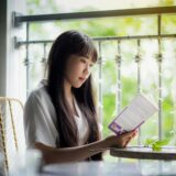 A serene portrait of a woman reading a book on a sunny balcony, surrounded by greenery.