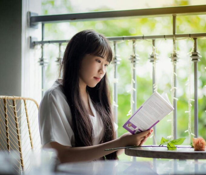 A serene portrait of a woman reading a book on a sunny balcony, surrounded by greenery.