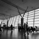 Black and white view of a busy airport terminal with travelers waiting and walking.