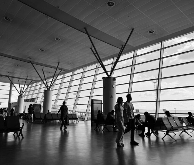 Black and white view of a busy airport terminal with travelers waiting and walking.