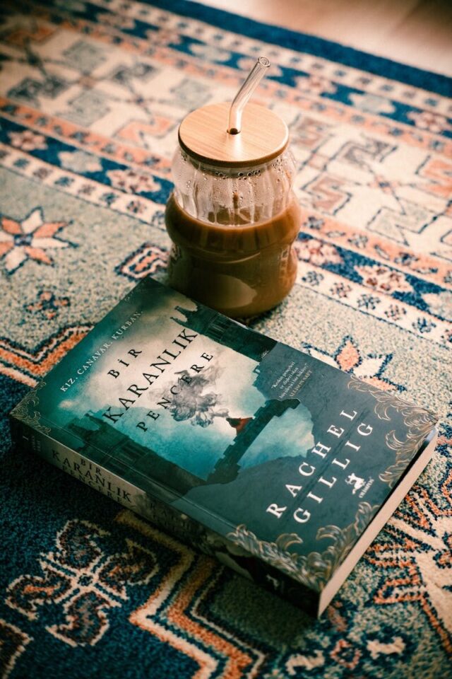 A relaxing setup with a novel and iced coffee on a patterned rug, perfect for book lovers.