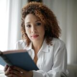Portrait of a woman with curly hair reading a book indoors, conveying relaxation and wisdom.