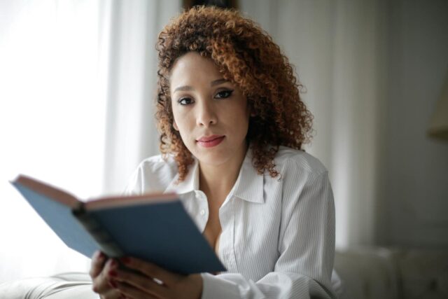 Portrait of a woman with curly hair reading a book indoors, conveying relaxation and wisdom.