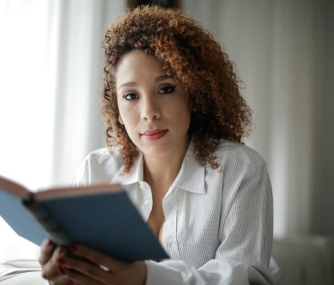 Portrait of a woman with curly hair reading a book indoors, conveying relaxation and wisdom.