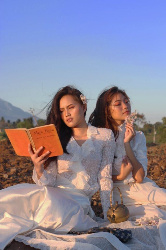 Two women in white dresses reading outdoors at sunset, embodying serenity and elegance.
