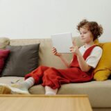 Young child engaged in online learning while comfortably seated on the sofa with a tablet.