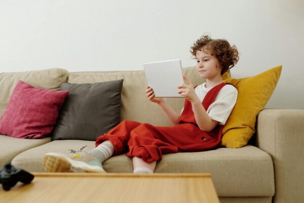 Young child engaged in online learning while comfortably seated on the sofa with a tablet.