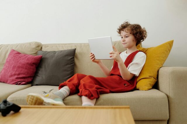 Young child engaged in online learning while comfortably seated on the sofa with a tablet.