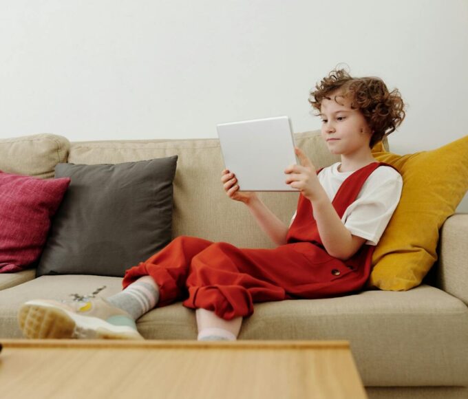 Young child engaged in online learning while comfortably seated on the sofa with a tablet.