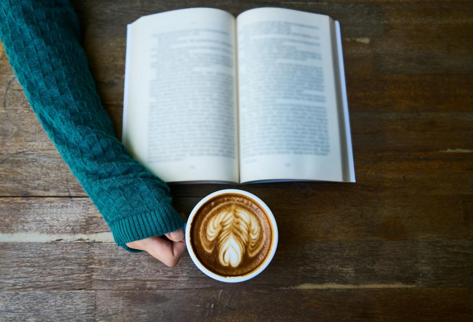 A cozy moment of reading a book with a latte art coffee in a warm café setting for relaxation.