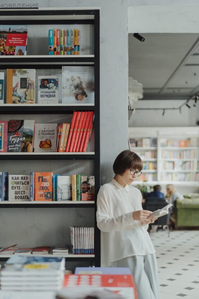 Young woman reading by a bookshelf in a contemporary bookstore setting.