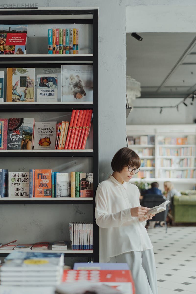 Young woman reading by a bookshelf in a contemporary bookstore setting.