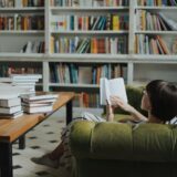 Woman reading on a sofa in a cozy library surrounded by book stacks.