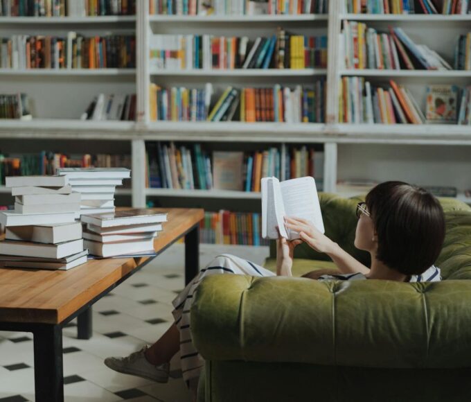 Woman reading on a sofa in a cozy library surrounded by book stacks.