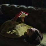 A young woman lies on a green sofa reading a red book, enjoying leisure indoors.