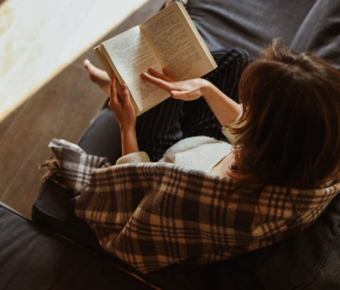 Woman relaxing with a book on a cozy sofa bathed in sunlight.