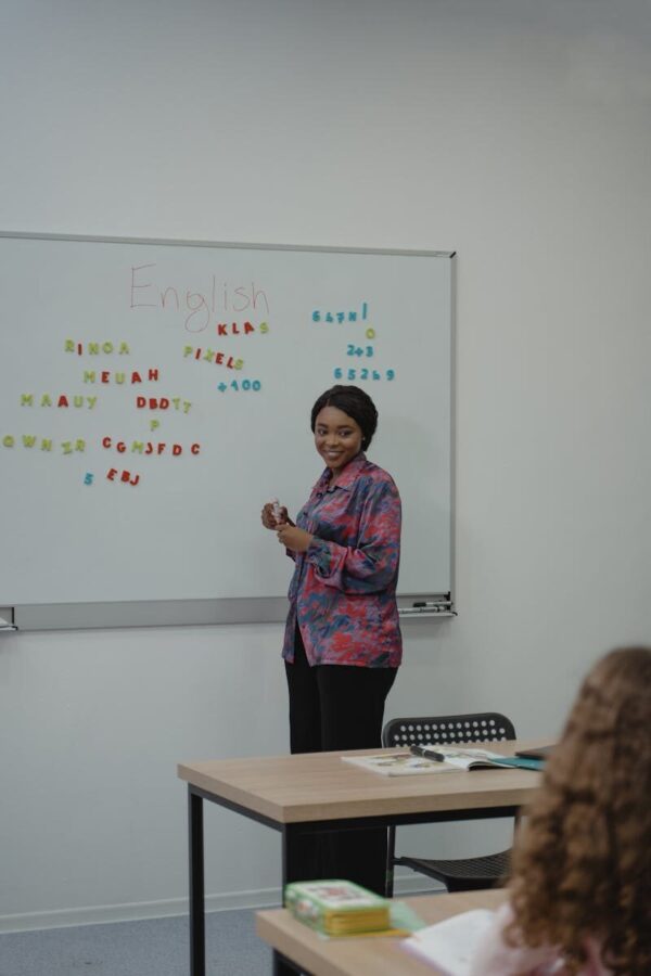 A female teacher explaining an English lesson to students in a classroom with a whiteboard.