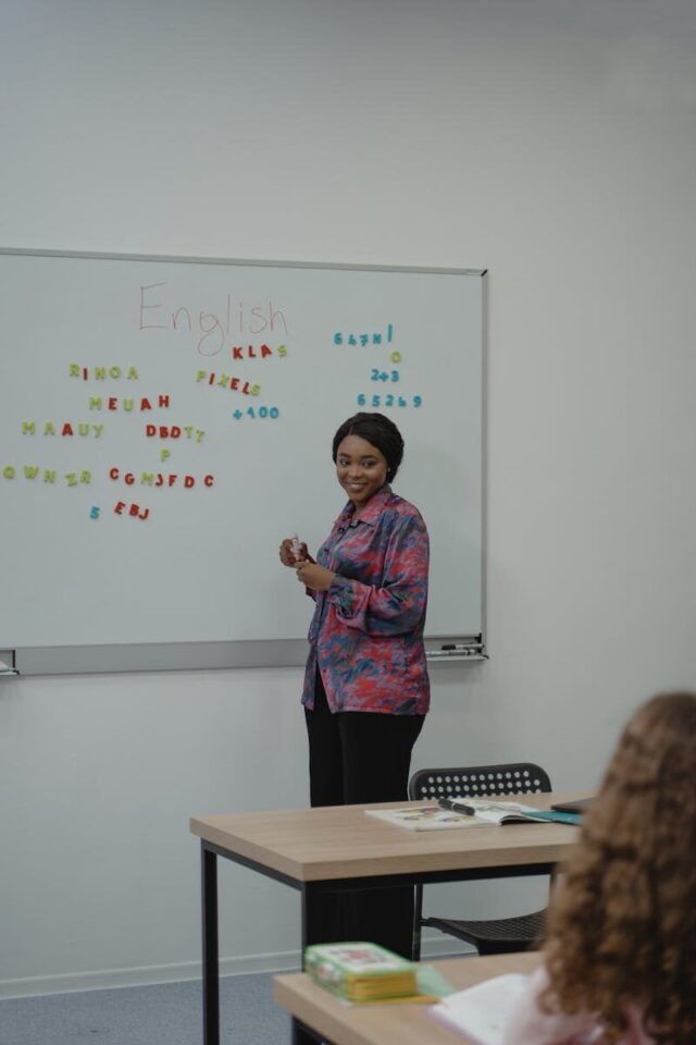A female teacher explaining an English lesson to students in a classroom with a whiteboard.