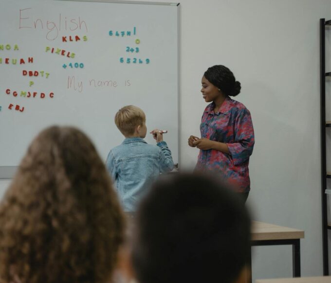 A teacher engages students in an interactive English lesson using a whiteboard and magnetic letters.