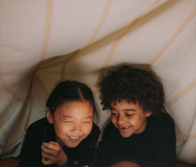 Two children happily reading under a cozy blanket fort with warm lighting.