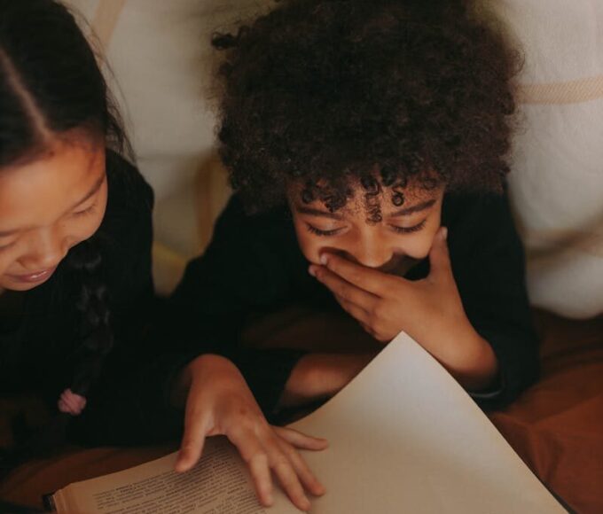 Two children enjoy reading a book together in a dimly lit, cozy tent setting.