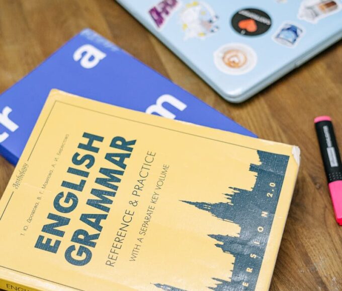 High-angle view of an English grammar book and a laptop with stickers on a wooden desk.