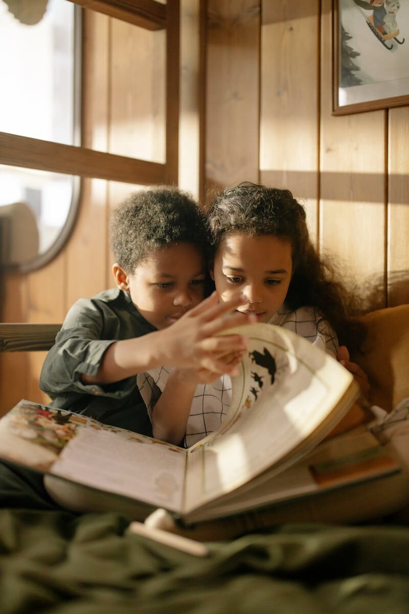 Two children reading a book together on a cozy couch by the window.