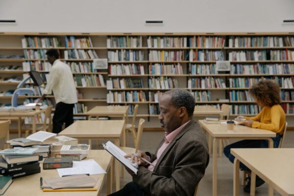 Adults reading and studying in a bright, modern library with a focus on education and diversity.