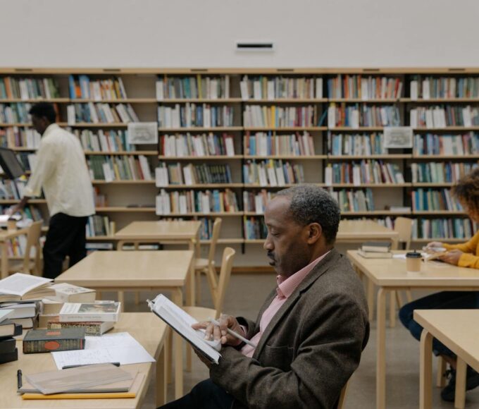 Adults reading and studying in a bright, modern library with a focus on education and diversity.