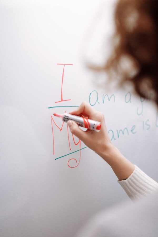 A hand with a marker writing on a whiteboard indoors. Educational context.